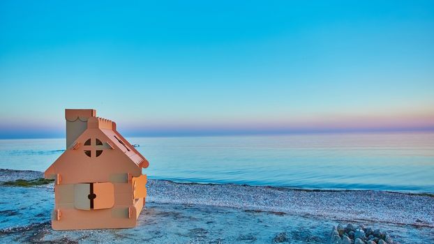 Toy house made of corrugated cardboard in the sea coast at sunset. The concept of eco-estate