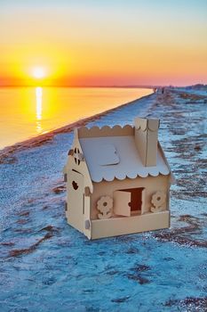 Toy house made of corrugated cardboard in the sea coast at sunset. The concept of eco-estate