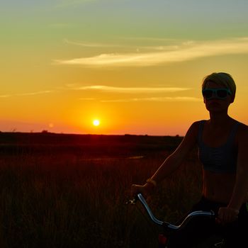 Biker girl at the sunset on the meadow