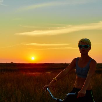 Biker girl at the sunset on the meadow