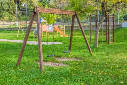 empty swings at playground for child near children stairs slides equipment, on green meadow background