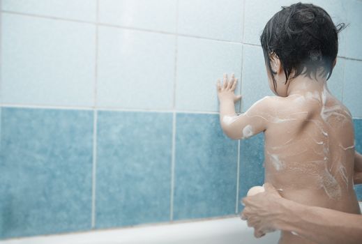 Mothers hands lathering child in the bath. Horizontal photo