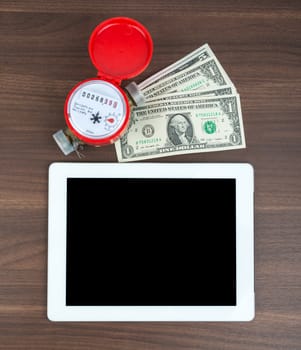 Tablet with money and water meter on wooden table