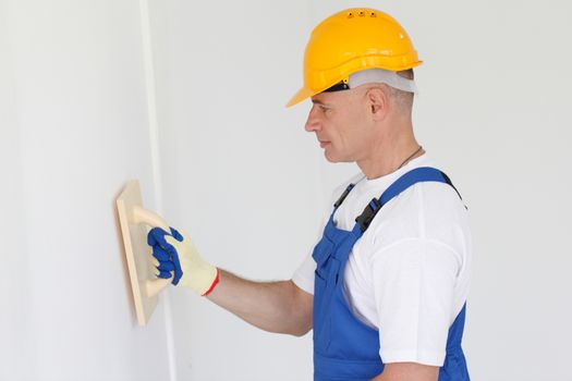 Portrait of workman wearing a yellow safety helmet polishing wall