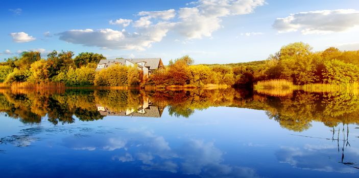 House in autumn forest near calm river