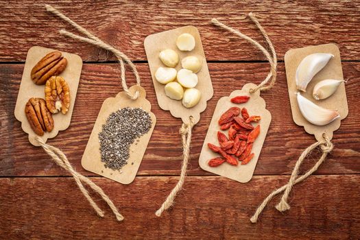 a variety of superfood (garlic, goji berry, chia seeds, macadamia and pecan nuts) on paper price tags against grunge barn wood background