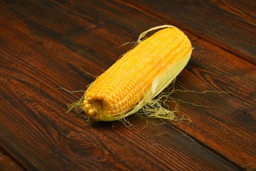 One open fresh yellow corn cob with green husk on dark brown vintage wooden surface