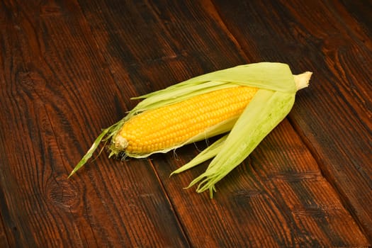 One open fresh yellow corn cob with green husk on dark brown vintage wooden surface