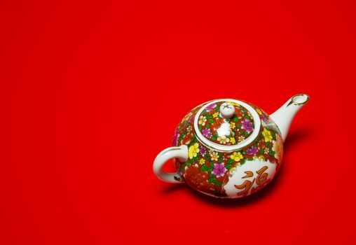 Chinese porcelain jug for tea and coffe with painted colorful flowers on an isolated red background.Horizontal view.