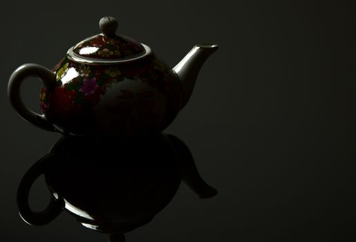 Chinese jug with a mirror image, on a black background with light reflections. Close horizontal view.