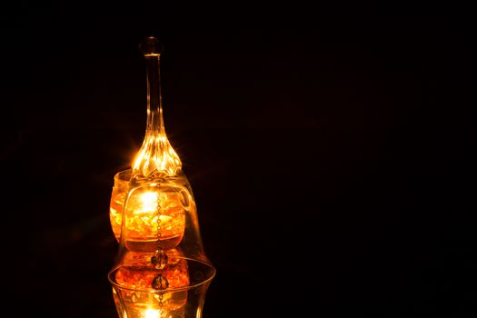 Ornate glass bell, candle lit from the back isolated on a black background with multiple light reflections and mirror reflection from the bottom. Horizontal view.