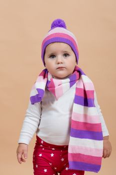 portrait of young cute baby with winter cap and scarf on beige background