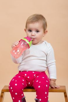 portrait of young cute baby with on beige background with bottle