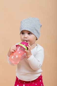 portrait of young cute baby with cap on head on beige background with bottle