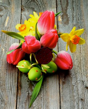 Arrangement of Yellow Daffodils, Magenta Tulips and Green Spotted Easter Eggs in Watering Can closeup on Rustic Wooden background