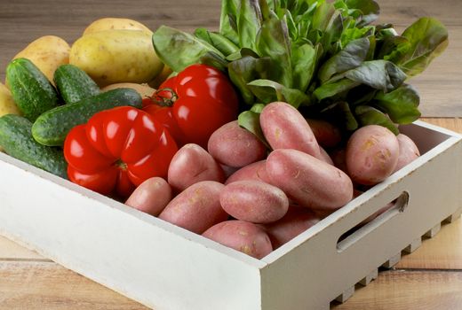 Arrangement of Raw Red and Yellow Potatoes, Cucumbers, Tomatoes and Butterhead Lettuce in White Wooden Box closeup on Rustic background