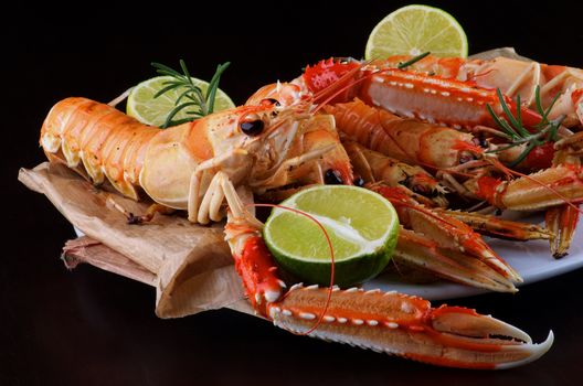 Delicious Grilled Langoustines with Lime and Rosemary on Parchment Paper in White Plate closeup on Dark Wooden background