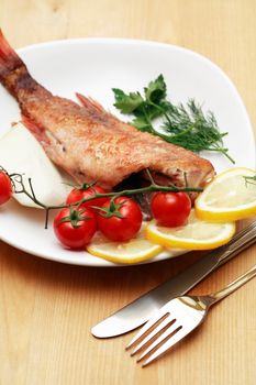 Mediterranean cousine. Plate with fried fish and vegetables near fork and knife