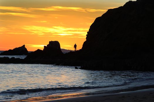 Silhouette of a man at sunset on a rock jetty at Shaw’s Cove in Laguna Beach, Southern California
