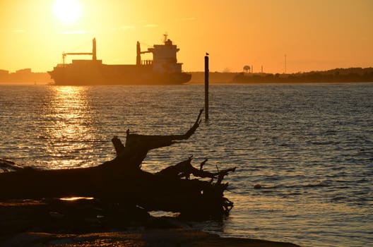 A cargo ship heading out to sea at sunset.