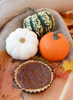 Small pumpkin pie with autumn leaves and gourds amongst burlap fabric