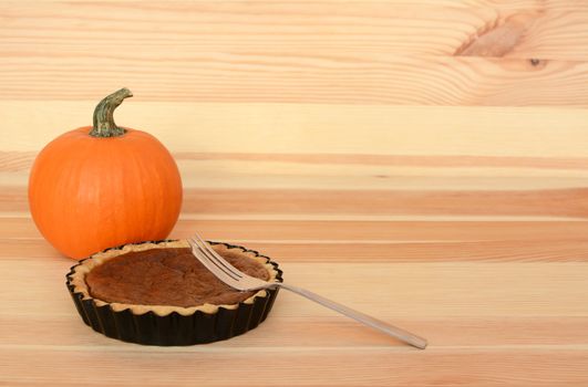 Fork with a small pumpkin pie on a wooden table with small orange gourd, with copy space