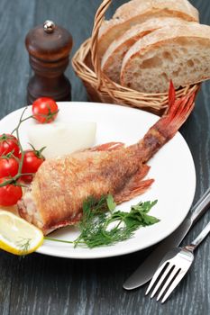 Mediterranean cuisine. Plate with fried fish and vegetables near fork and knife