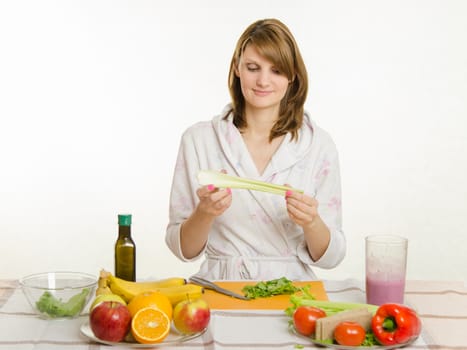 Young beautiful girl in a bathrobe prepares vegetarian salad from vegetables and greens isolated on white background