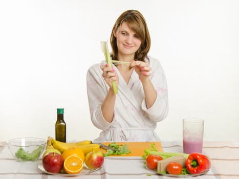 Young beautiful girl in a bathrobe prepares vegetarian salad from vegetables and greens isolated on white background