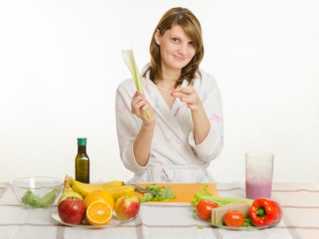 Young beautiful girl in a bathrobe prepares vegetarian salad from vegetables and greens isolated on white background