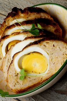 Slices of Delicious Homemade Meatloaf Stuffed with Boiled Eggs in Bowl closeup on Rustic Wooden background