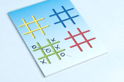 A close up of a game of Xs and Os on a note pad with colorful grids made for playing.