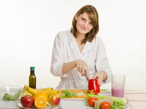 Young beautiful girl in a bathrobe prepares vegetarian salad from vegetables and greens isolated on white background