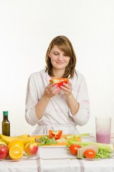 Young beautiful girl in a bathrobe prepares vegetarian salad from vegetables and greens isolated on white background