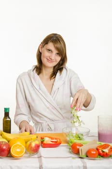 Young beautiful girl in a bathrobe prepares vegetarian salad from vegetables and greens isolated on white background