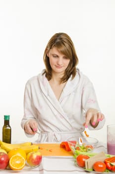 Young beautiful girl in a bathrobe prepares vegetarian salad from vegetables and greens isolated on white background