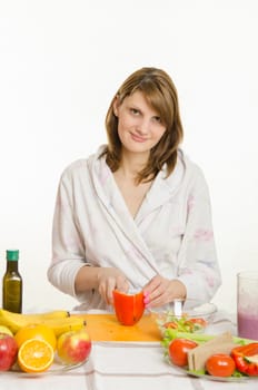 Young beautiful girl in a bathrobe prepares vegetarian salad from vegetables and greens isolated on white background