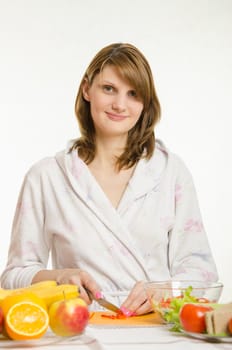 Young beautiful girl in a bathrobe prepares vegetarian salad from vegetables and greens isolated on white background