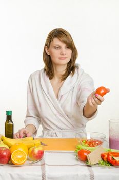 Young beautiful girl in a bathrobe prepares vegetarian salad from vegetables and greens isolated on white background