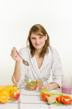 Young beautiful girl in a bathrobe prepares vegetarian salad from vegetables and greens isolated on white background