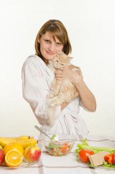 Young beautiful girl in a bathrobe prepares vegetarian salad from vegetables and greens isolated on white background