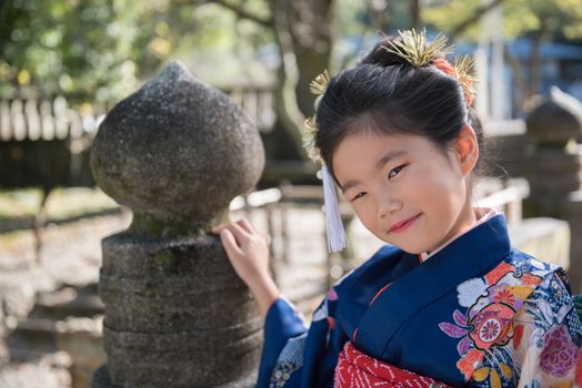 A young Japanese girl in a kimono outdoors at a shrine.