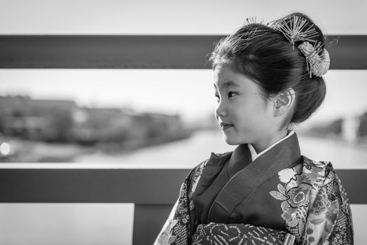 A young Japanese girl in a kimono outdoors on a bridge over a river.