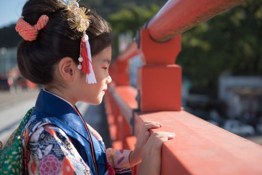 A young Japanese girl in a kimono outdoors on a bridge.