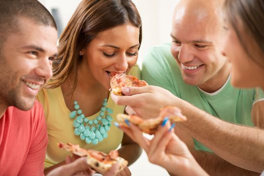 Close up of a young girl smiling and eating pizza with her friends.
