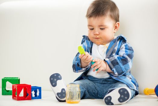 Cute baby boy sitting at home and playing with spoon