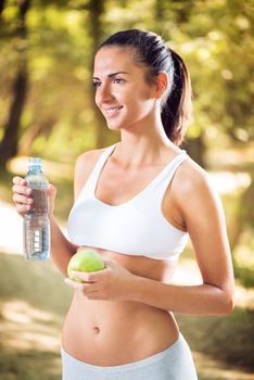 Young beautiful woman with apple and water bottle  in the nature