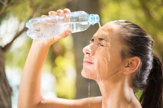 Young beautiful woman refreshing in the nature. She is refreshed with water from a bottle.