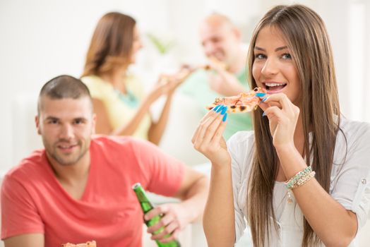 Close up of a young girl smiling and eating pizza with her friends in the background.