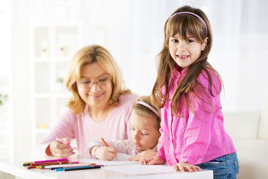 Two cute little girls drawing with colored pencils at home with grandmother
